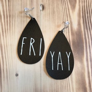 Puede incluir: Un par de pendientes de cuero negro en forma de l&aacute;grima con letras blancas. El pendiente izquierdo dice "FRI" y el derecho dice "YAY".