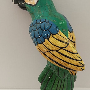 May include: A green, blue, and yellow painted wooden parrot figurine. The parrot is facing left and has a black beak and white eye.