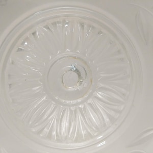 May include: A white glass ceiling light fixture with a decorative floral pattern. The center of the fixture has a circular opening for a light bulb.