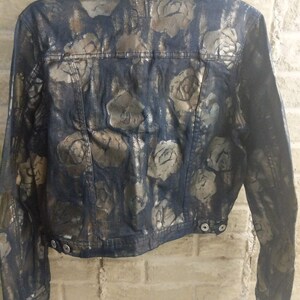 May include: A dark blue denim jacket with a gold metallic rose print. The jacket has a button-up front and long sleeves.