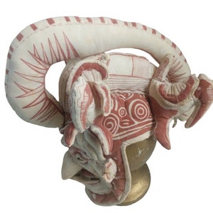 Könnte beinhalten: Ein roter und weißer Stoffhelm mit einem großen, gebogenen Horn oben. Der Helm ist mit komplizierten Mustern und Designs verziert.