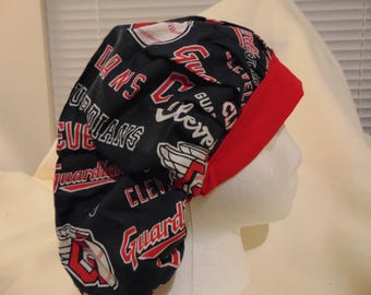 May include: A black and red scrub cap featuring the Cleveland Guardians baseball team logo and text. The cap has a red band and is designed to cover the head. The baseball-themed cap is made of fabric.