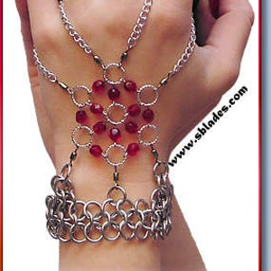 May include: A silver chain bracelet with red beads and a chainmail cuff. The bracelet is designed to be worn on the hand and has multiple chains that connect to the cuff.