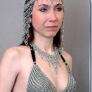 May include: A silver chainmail top with a matching silver chainmail headpiece. The headpiece has a pointed crown and is decorated with small, clear crystals.