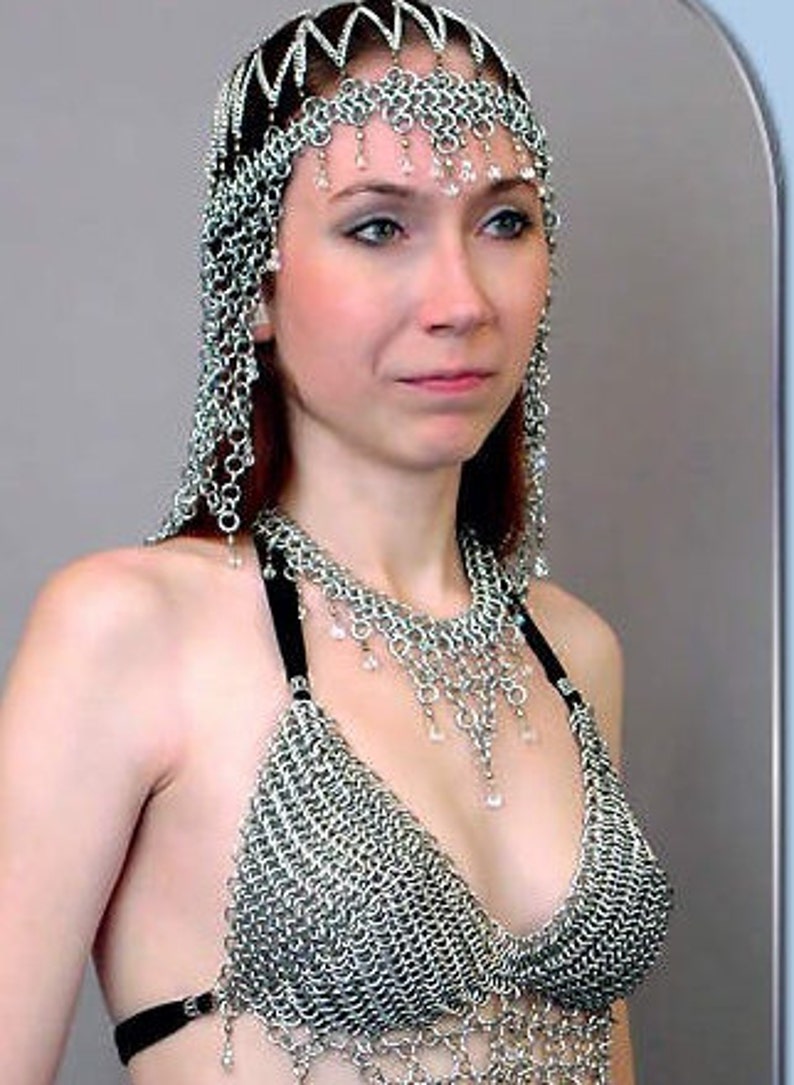 May include: A silver chainmail top with a matching silver chainmail headpiece. The headpiece has a pointed crown and is decorated with small, clear crystals.