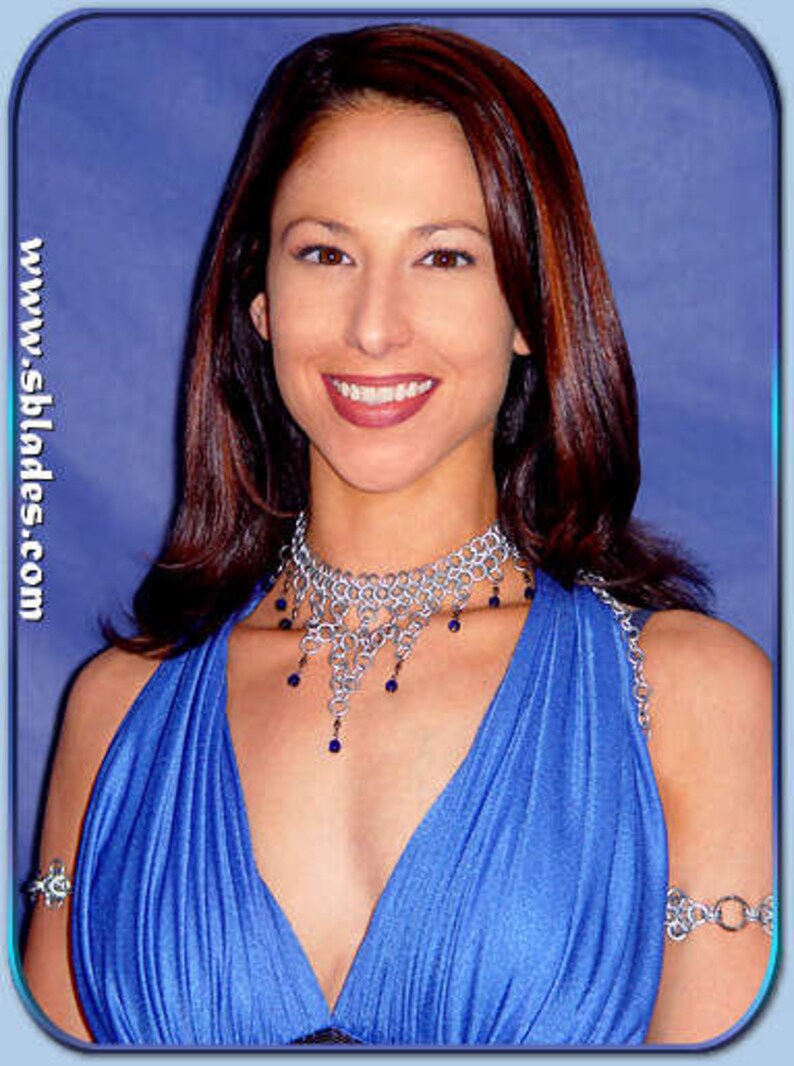 May include: A woman wearing a blue dress with a silver chainmail necklace and matching bracelets. The necklace has blue beads hanging from it.