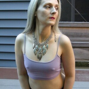 May include: A woman with long, silver hair is wearing a purple tank top and a silver necklace with leaf-shaped pendants.