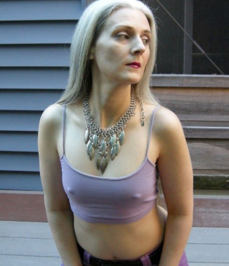 May include: A woman with long, silver hair is wearing a purple tank top and a silver necklace with leaf-shaped pendants.
