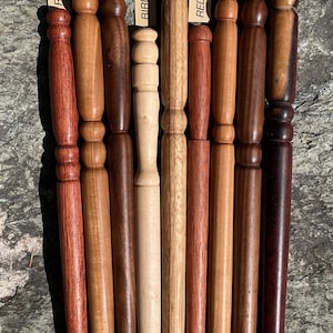 May include: A collection of nine turned wooden wands arranged vertically, each featuring a unique wood grain and color. Labels identify the wood types as Red Oak, Oak, Walnut, Birdseye Maple, Zebra, Red Oak, Oak, Walnut, and Cocobolo.