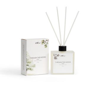 May include: A square, frosted glass reed diffuser with a black cap and four white reeds, accompanied by a rectangular white box. Both items feature the text "Through the Woods" and "Reed Diffuser" along with a small illustration of pine branches.