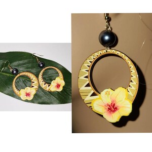 May include: A pair of gold hoop earrings with a yellow hibiscus flower and a black bead dangle. The earrings are made of wood and have a geometric pattern.