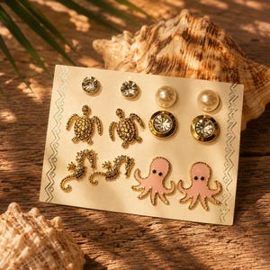 May include: A set of six pairs of stud earrings on a display card. The collection includes clear crystal studs, white pearl studs, gold-tone crystal studs, gold-tone sea turtle studs, gold-tone seahorse studs, and light pink enamel octopus studs.