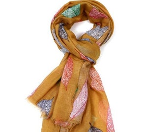 May include: A mustard yellow scarf with a colorful leaf pattern. The leaves are outlined in black and filled with shades of pink, red, green, and blue.