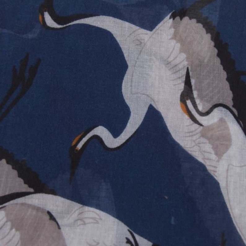 May include: A navy blue fabric with a white crane pattern. The crane is in flight with its wings spread out. The fabric has a soft, flowing texture.