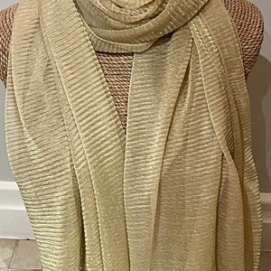 May include: A gold metallic scarf with a crinkled texture. The scarf is draped over a straw mannequin.