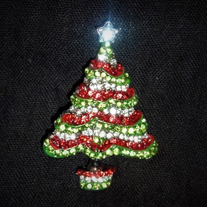 Könnte beinhalten: Eine funkelnde Weihnachtsbaum-Brosche mit roten und grünen Strasssteinen und einem silbernen Stern oben.