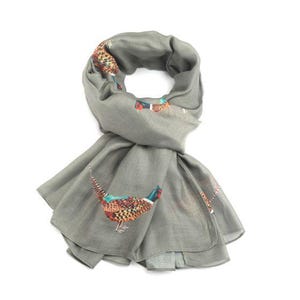 Peut inclure: Une écharpe grise ornée d'un motif de faisan. L'écharpe est faite d'une matière douce et présente une impression détaillée de faisans colorés. Les plumes du faisan sont dans des tons de marron, orange, bleu et vert.