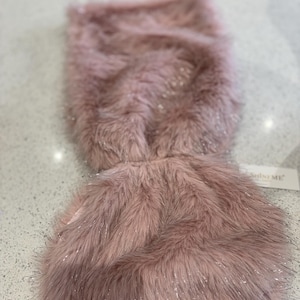 May include: A fluffy, pink faux fur scarf with silver glitter accents. The scarf is rectangular with a rounded bottom and a tag that reads "Shine ME". The soft, plush material is ideal for adding a touch of glamour to any outfit.