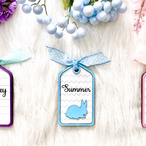 May include: Three wooden gift tags with bunny silhouettes and personalized names: Sydney, Summer, and Sienna. Each tag is decorated with a different pattern and color: purple, blue, and pink.