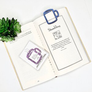 May include: A purple and white coffee mug bookmark with the text "Book Coffee Repeat" on a book with a blue mug bookmark. The book is open to a page with the title "Stumbling" and a quote by Willa Cather.