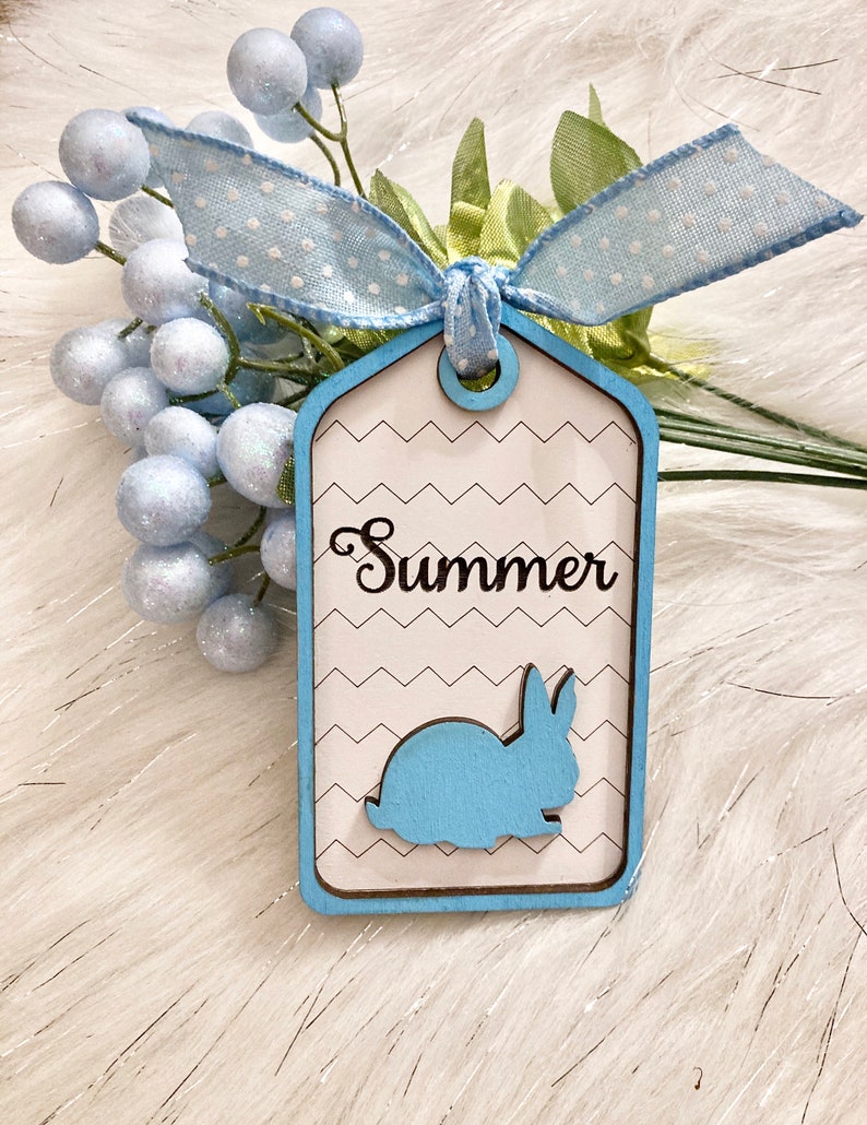 May include: A blue and white wooden tag with a white chevron pattern. The tag has a blue bunny silhouette and the word "Summer" written in black cursive.
