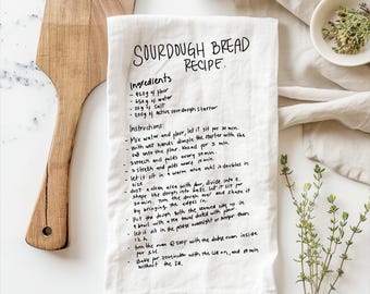 May include: A white tea towel with a handwritten sourdough bread recipe. The recipe includes ingredients like flour, water, salt, and active sourdough starter. The instructions include mixing, kneading, stretching, and baking the bread.