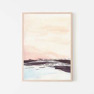 Peut inclure: Une peinture &agrave; l'aquarelle encadr&eacute;e d'un paysage avec un ciel rose et orange et un premier plan bleu fonc&eacute; et gris. La peinture est dans un cadre en bois clair.