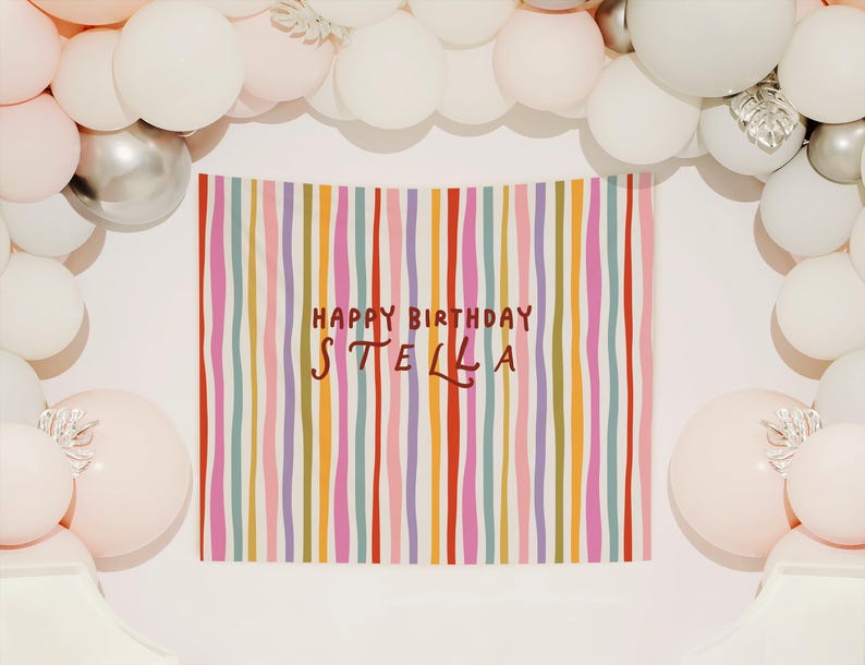 May include: A colorful birthday banner with vertical stripes in various colors, including red, pink, and purple, with the text "HAPPY BIRTHDAY STELLA". The banner is surrounded by white, silver, and pink balloons, creating a festive party atmosphere.