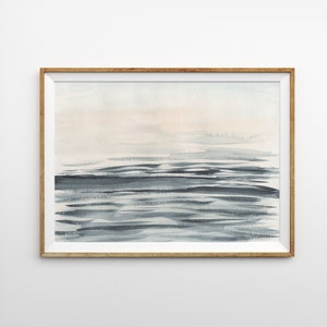 Puede incluir: Una pintura de acuarela enmarcada de un paisaje mar&iacute;timo con colores suaves y apagados. La pintura presenta un cielo azul claro con un toque de rosa y un oc&eacute;ano azul oscuro con olas sutiles.