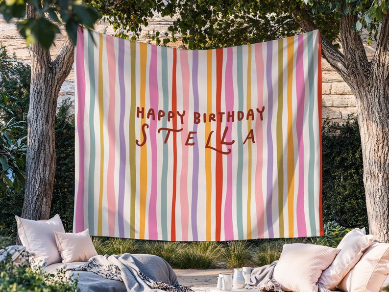 May include: A colorful birthday banner with vertical stripes in various colors, including pink, yellow, and green. The words "HAPPY BIRTHDAY STELLA" are written in a brown, handwritten-style font.
