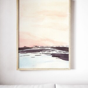 Peut inclure: Une peinture &agrave; l'aquarelle encadr&eacute;e d'un paysage avec un ciel rose et orange, une &eacute;tendue d'eau bleu fonc&eacute; et une masse terrestre gris fonc&eacute; au premier plan.