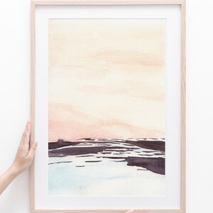 Peut inclure: Une peinture &agrave; l'aquarelle encadr&eacute;e d'un paysage marin avec un ciel rose p&acirc;le et orange, une eau bleu fonc&eacute; et un rivage brun fonc&eacute;.