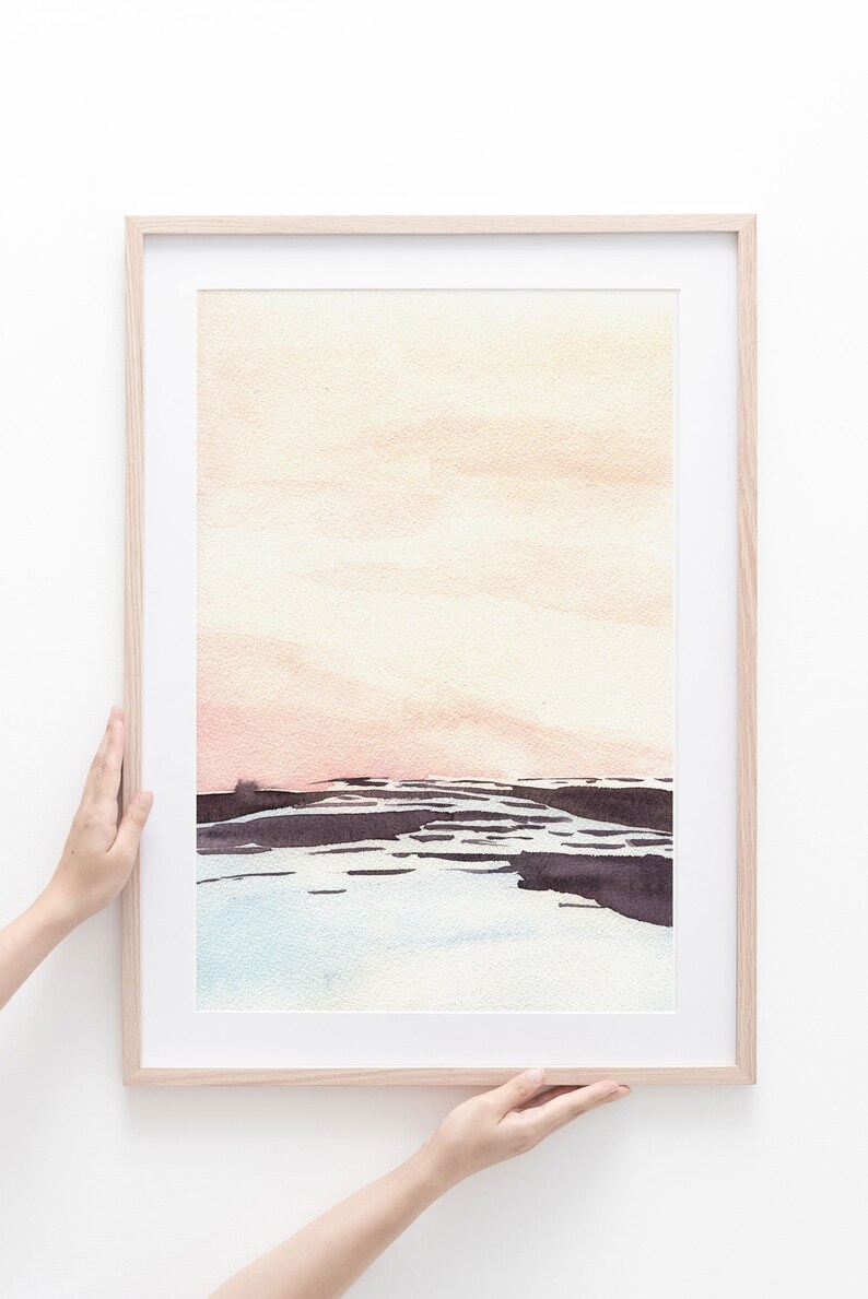 Peut inclure: Une peinture &agrave; l'aquarelle encadr&eacute;e d'un paysage marin avec un ciel rose p&acirc;le et orange, une eau bleu fonc&eacute; et un rivage brun fonc&eacute;.