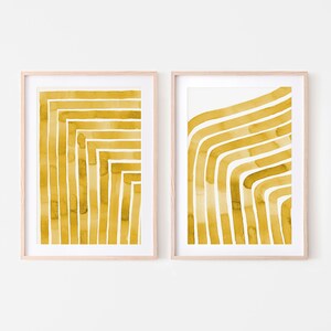 May include: Two framed prints with abstract watercolor designs in a mustard yellow color. The designs are made up of thick, curved lines.
