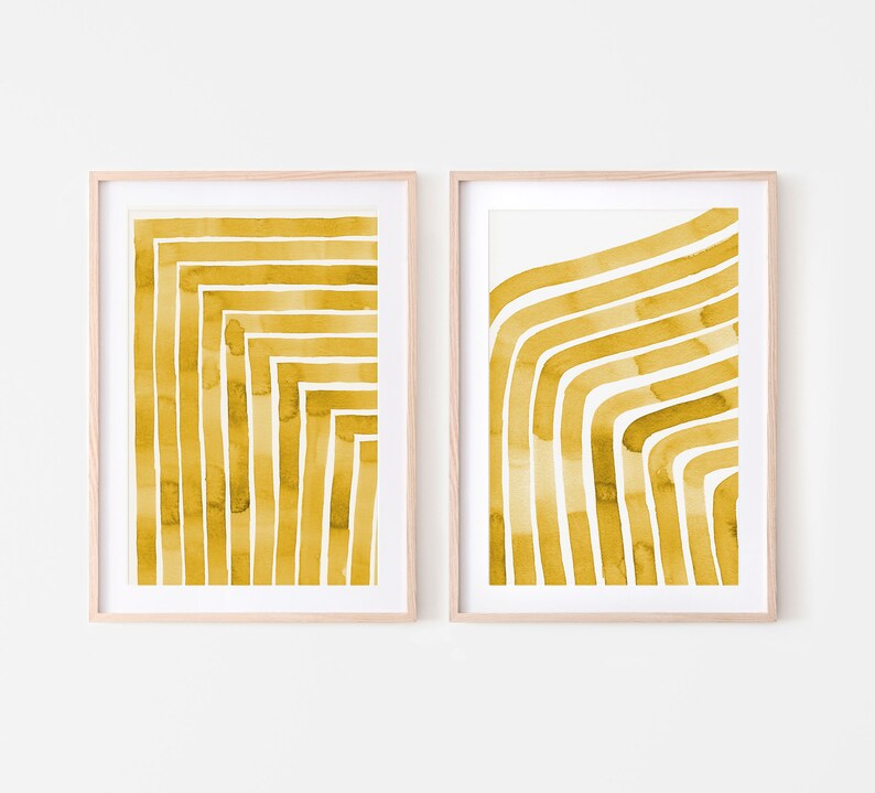 May include: Two framed prints with abstract watercolor designs in a mustard yellow color. The designs are made up of thick, curved lines.