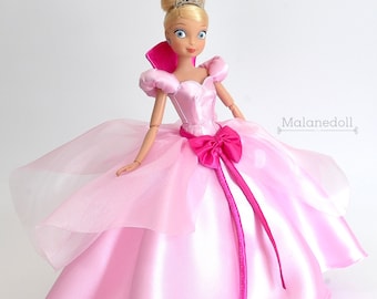 May include: A pink satin and tulle ball gown with a pink bow and a tiara on a blonde doll.