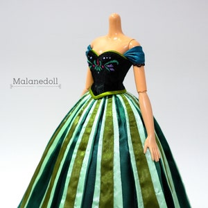 May include: A doll wearing a green and black dress with a striped skirt. The dress has a black bodice with a floral design and a green sash.