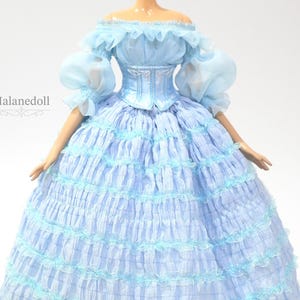 K&ouml;nnte beinhalten: Hellblaues Puppenkleid mit schulterfreiem Ausschnitt und ger&uuml;schten &Auml;rmeln. Das Kleid hat ein figurbetontes Oberteil und einen vollen, mehrlagigen Rock mit zarten Verzierungen. Das Puppenkleid ist im Vintage-Stil gehalten.
