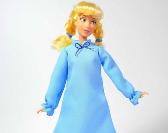 May include: A blonde doll wearing a light blue nightgown with a black bow at the neckline. The doll has a white background.