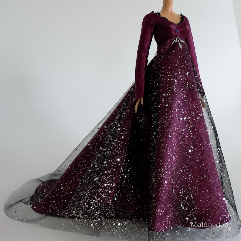 Puede incluir: Un vestido de terciopelo burdeos con una superposici&oacute;n de tul negro y detalles de purpurina plateada. El vestido tiene mangas largas y un corpi&ntilde;o ajustado. La falda es amplia y fluida.