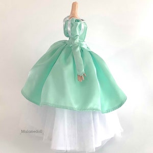 Puede incluir: Un vestido de bola de sat&eacute;n verde menta con una falda interior de tul blanco. El vestido tiene mangas abullonadas con ribete de cinta de sat&eacute;n blanco. El vestido est&aacute; en un maniqu&iacute; de tama&ntilde;o de mu&ntilde;eca.