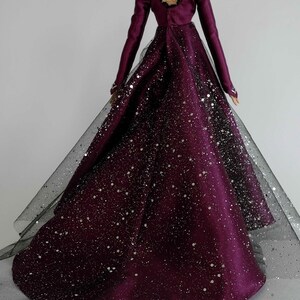 Puede incluir: Un vestido largo de color burdeos con una superposici&oacute;n de tul negro y purpurina plateada. El vestido tiene la espalda baja con un detalle de encaje negro.