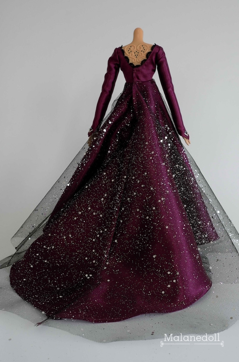 Puede incluir: Un vestido largo de color burdeos con una superposici&oacute;n de tul negro y purpurina plateada. El vestido tiene la espalda baja con un detalle de encaje negro.