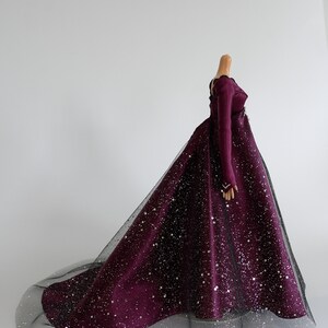 Puede incluir: Un vestido largo de color burdeos con una superposici&oacute;n de tul negro y purpurina plateada. El vestido tiene mangas largas y un corpi&ntilde;o ajustado.