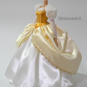 May include: A white and gold satin ball gown with a gold bodice and white puffed sleeves. The gown has a gold trim around the bottom.