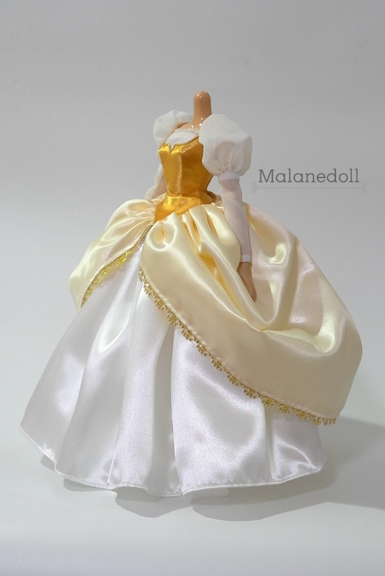 May include: A white and gold satin ball gown with a gold bodice and white puffed sleeves. The gown has a gold trim around the bottom.