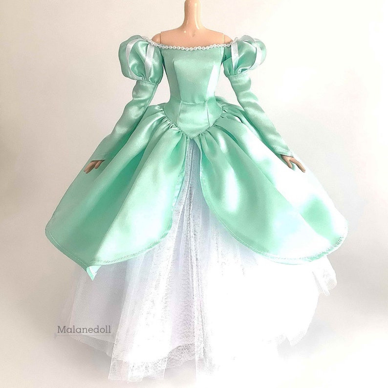 Puede incluir: Un vestido de bola de sat&eacute;n verde menta con una falda de tul blanca. El vestido tiene un escote de coraz&oacute;n y mangas largas con hombros abullonados. El corpi&ntilde;o es ajustado y la falda es completa y fluida.