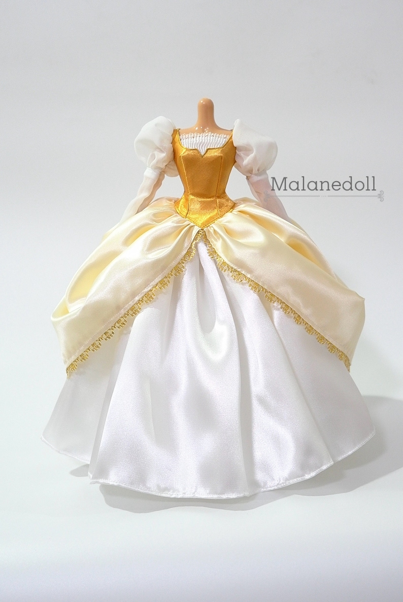 May include: A white and gold satin ball gown with a gold bodice and puffy white sleeves. The gown has a gold trim around the bottom.