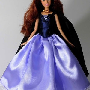 May include: A doll wearing a blue and purple dress with a black cape. The doll has long red hair and brown eyes.