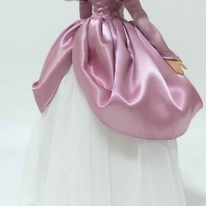Op de afbeelding: Een roze satijnen baljurk met een witte tule onderrok en witte satijnen lintaccenten op de pofmouwen.